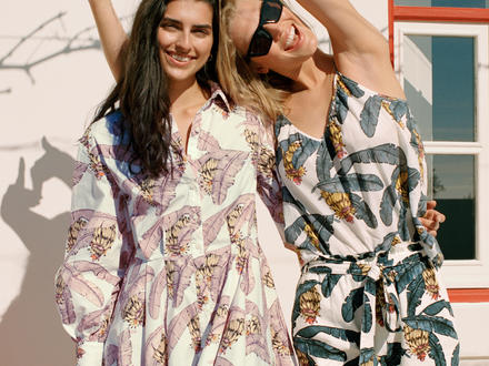 Two girls in palm-printed dresses outside smiling