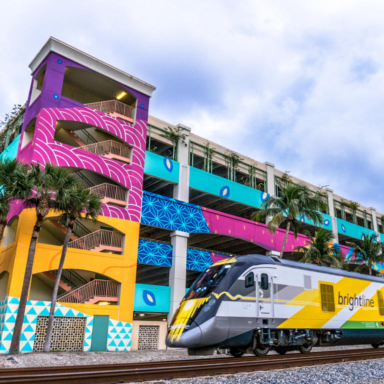 Brightline train passes by in front of brightly painted parking garage