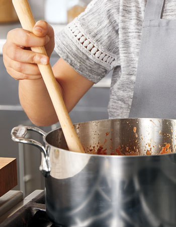 child stirring pasta sauce